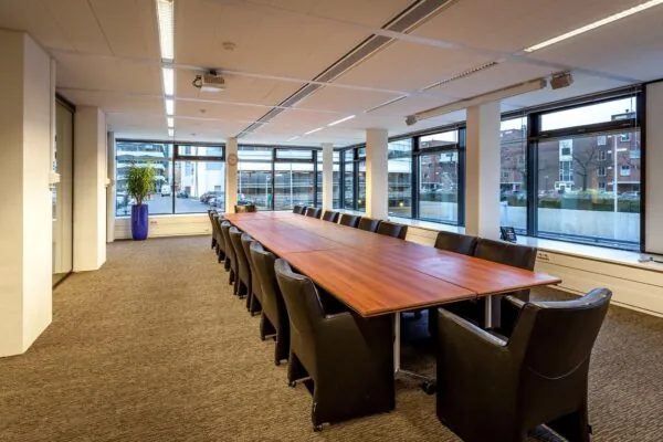 Vergaderruimte met lange houten tafel, omringd door zwarte stoelen, gelegen aan de Prinses Beatrixlaan.